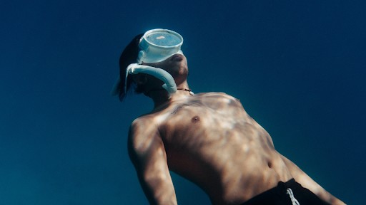 The man is wearing swimming goggles and appears to be in a streamlined position, suggesting active snorkeling