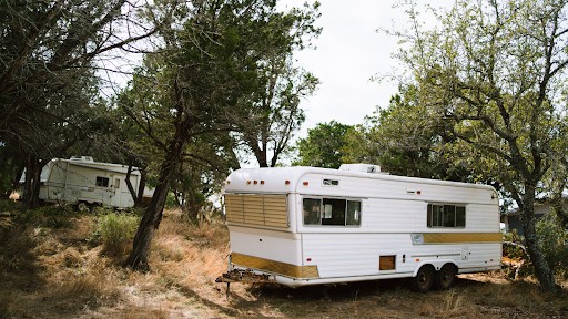 a recreational vehicle (RV), specifically a travel trailer, parked in a wooded or natural setting, suggesting a camping or outdoor living scenario