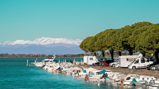 a scenic view of Grado Italy specifically showcasing a marina or waterfront area with boats and recreational vehicles RVs or campers parked nearby